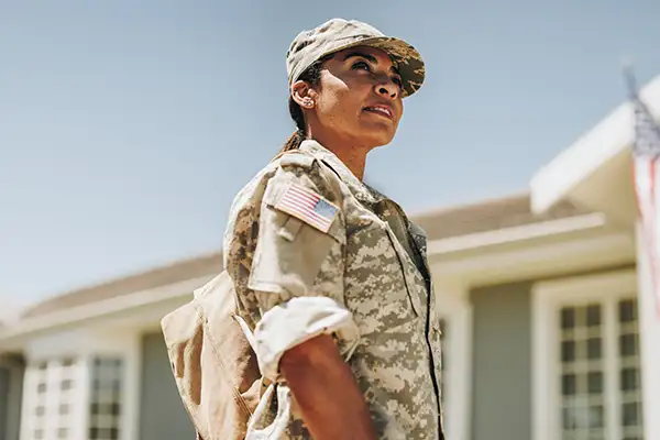 Soldier in US military uniform standing outside home with American flag