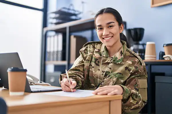 Young soldier wearing army uniform using laptop and writing on document in an office