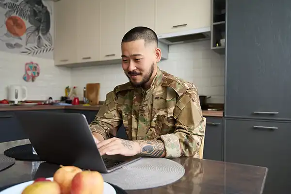 Soldier in US military uniform using laptop in kitchen