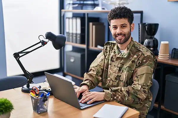 Young soldier in military uniform using laptop in an office