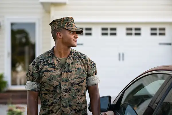 Soldier wearing US military uniform standing in front of house and near car