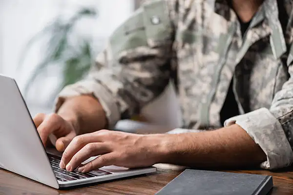 Man in military uniform typing on laptop